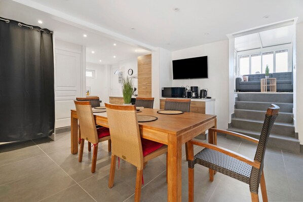 Ein stilvoller Essbereich mit Holztisch und Korbstühlen, eine Küche mit Flachbildfernseher und eine Treppe, die zu einem Balkon führt.