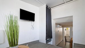 Un soggiorno moderno con una TV a schermo piatto montata al muro, una pianta in vaso e un tavolo di legno.