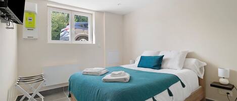 Hotelkamer met een bed, raam, radiator, bureau en lamp.