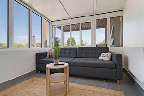 A modern living room with a grey sofa, a small wooden side table, and a potted plant.