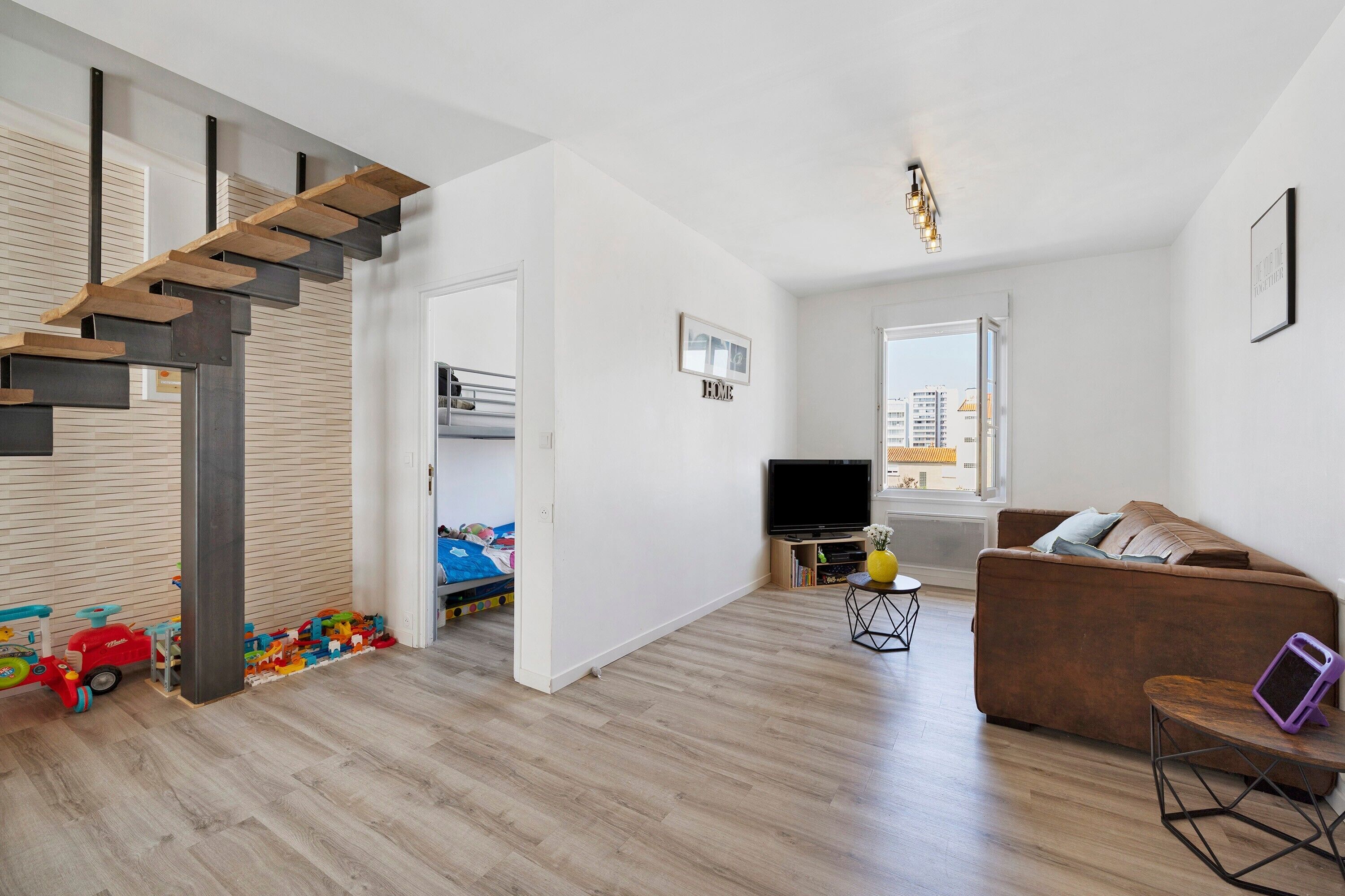 Ein modernes Wohnzimmer mit einer Holztreppe, einem Sofa, einem Fernseher und einem Bücherregal.