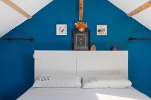 Une chambre avec un mur bleu, une tête de lit blanche, deux oreillers blancs et deux tableaux encadrés.