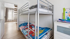 Een stapelbed met een kleurrijk dekbed, een witte kast met lades en een trap naar een andere kamer.