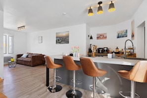 A modern kitchen with a central island, bar stools, and a dining area with a sofa. - Stay at "L'Ensoleillé" – City Center / Train Station (Les Sables-d'Olonne)