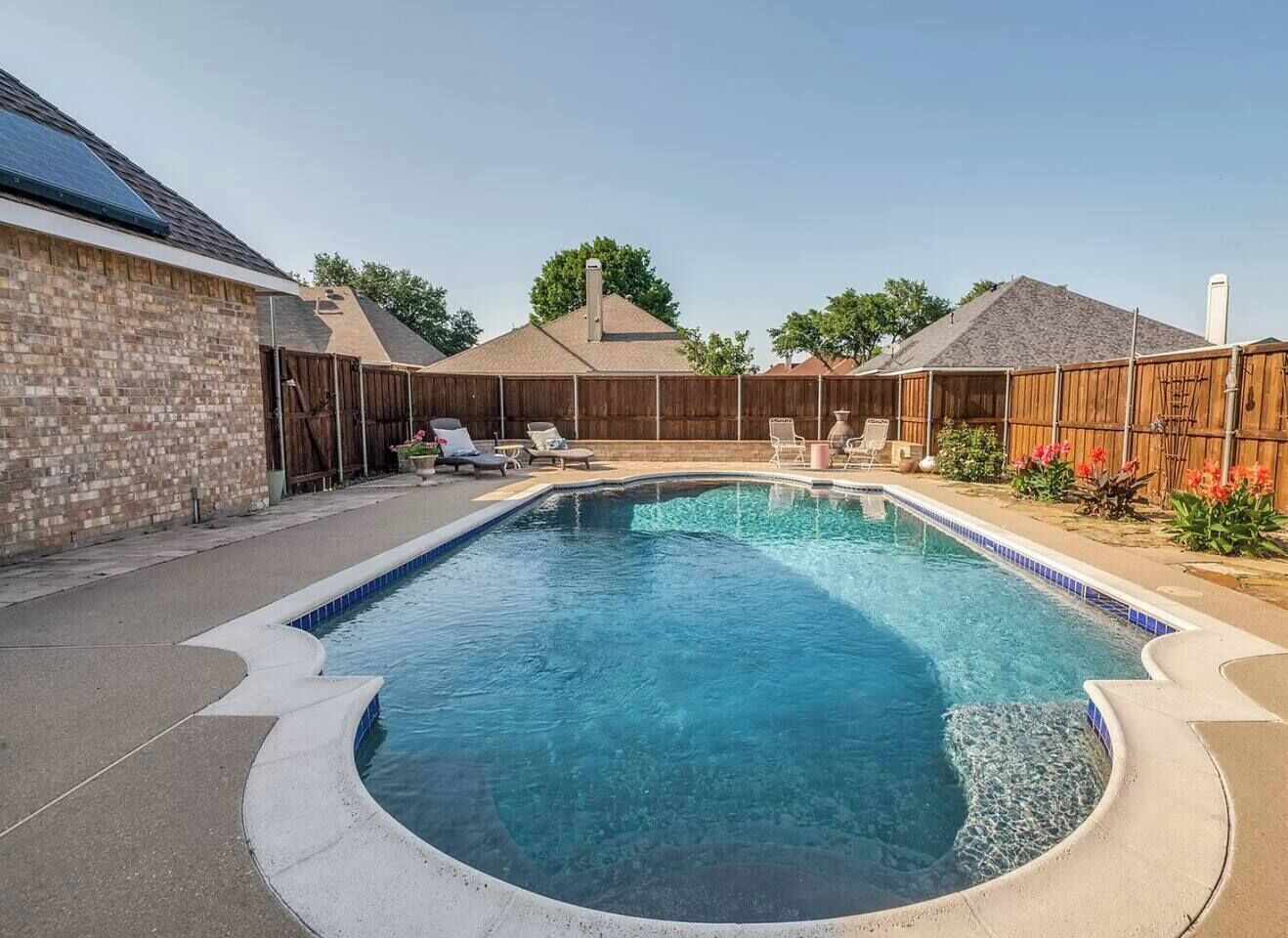 Una piscina rectangular con borde de azulejos, rodeada por un muro de ladrillo y una valla de madera.
