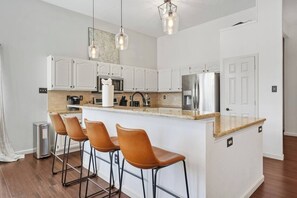 Eine moderne Küche mit weißen Schränken, einer Granit Arbeitsplatte, Edelstahlgeräten und drei Barhocker.