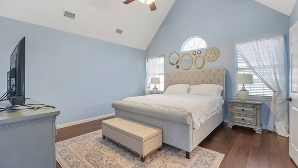 Quarto com cama, televisão, ventoinha no teto, janela com cortinas e um objeto decorativo na parede.