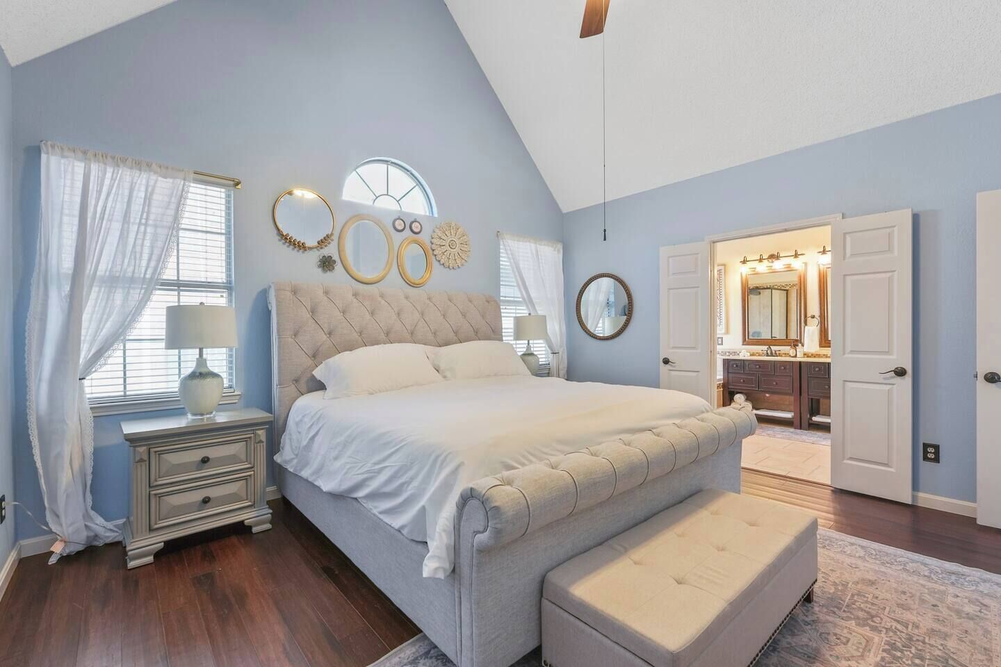 Quarto com uma cama grande, mesa de cabeceira, cômoda, penteadeira com espelho e porta para outro cômodo.