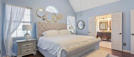 Quarto com uma cama grande, mesa de cabeceira, cômoda, penteadeira com espelho e porta para outro cômodo.