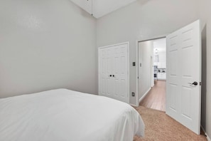 Ein Schlafzimmer mit einem Bett, zwei weißen Türen und einem zur Küche führenden Gang.