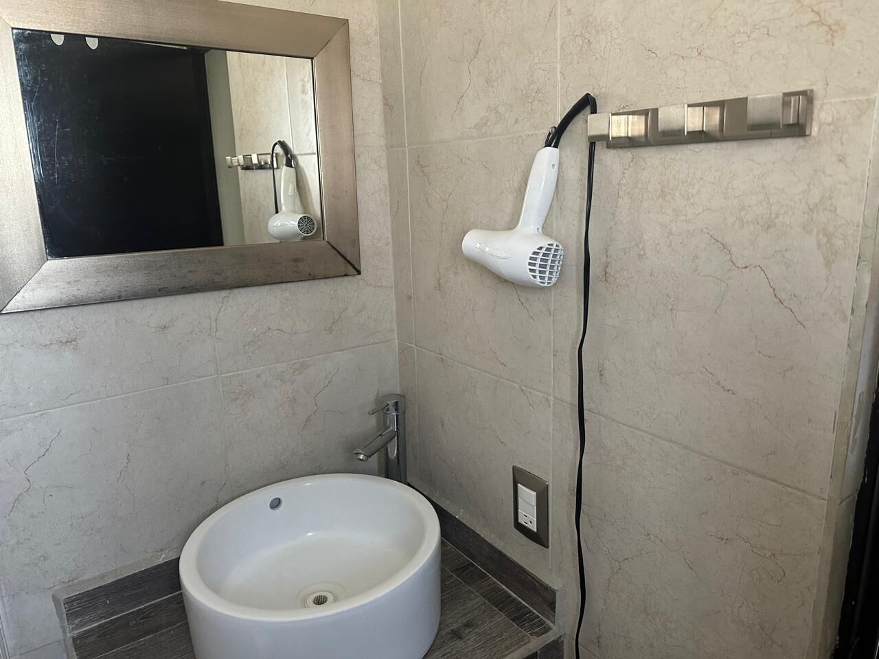 A bathroom with a sink, mirror, and hairdryer mounted on the wall.