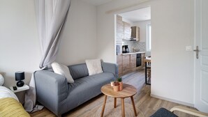 Ein modernes Wohnzimmer mit einem grauen Sofa, einem kleinen runden Holztisch und einer Küche im Hintergrund.