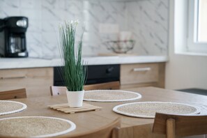 Een eettafel met een witte pot groene planten, houten onderzetters en placemats.