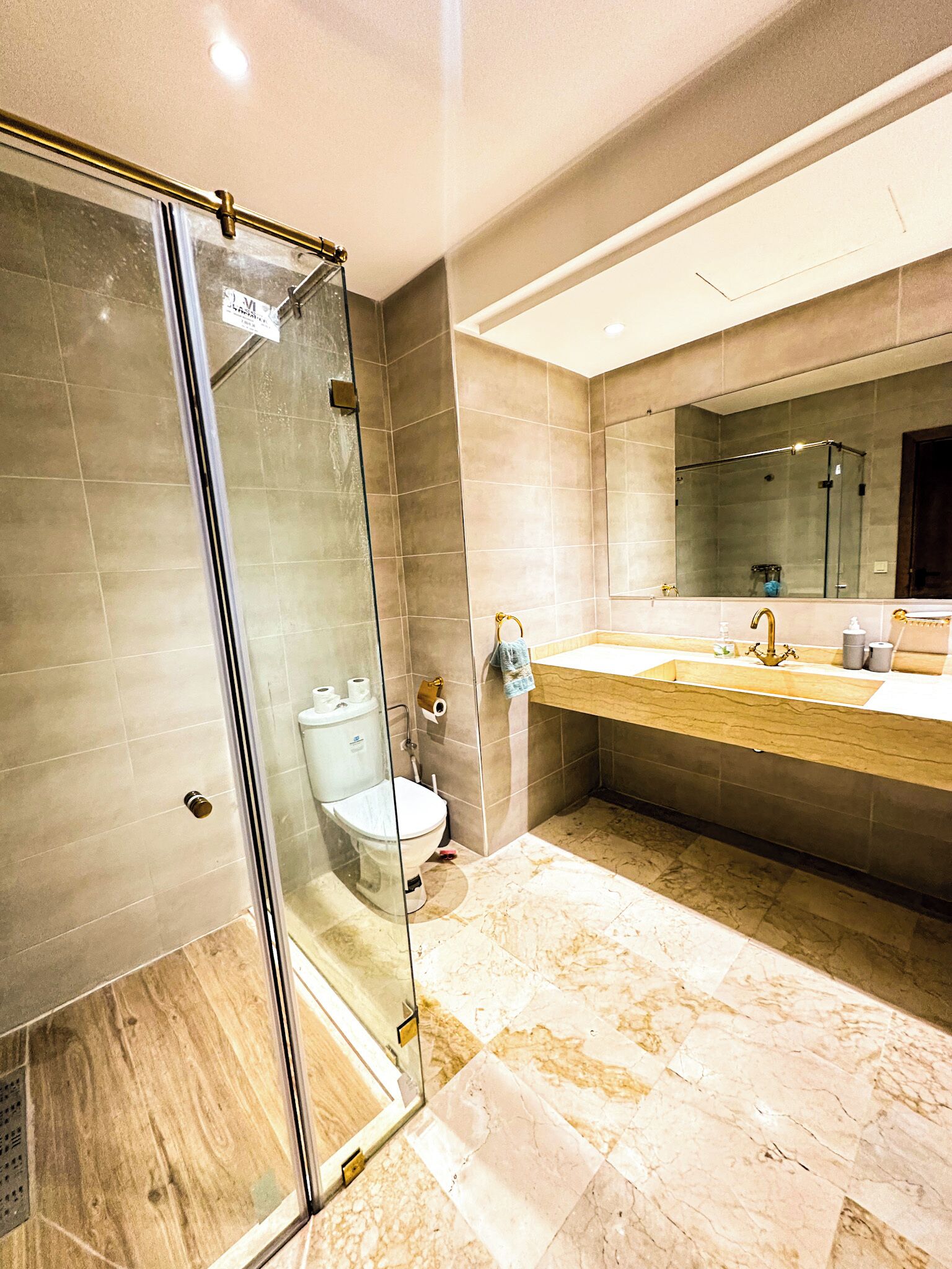 Ein modernes Badezimmer mit einer in Glas abgeschirmten Dusche, einem Marmorboden und einem großen Spiegel über dem Waschbecken.