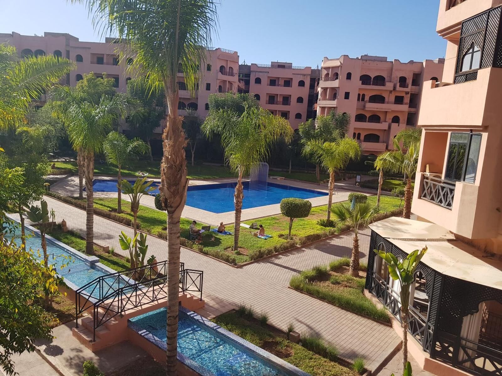 Zona de piscina amb palmeres, una piscina petita i un edifici amb balcons.