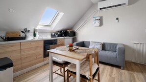 Een moderne keuken met dakraam, een eethoek met een houten tafel en stoelen, en een grijze bank in een woonruimte in loftstijl.