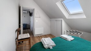 Een slaapkamer met een schuine kap, dakraam, een bed met groene sprei, een houten stoel en een droogrek.