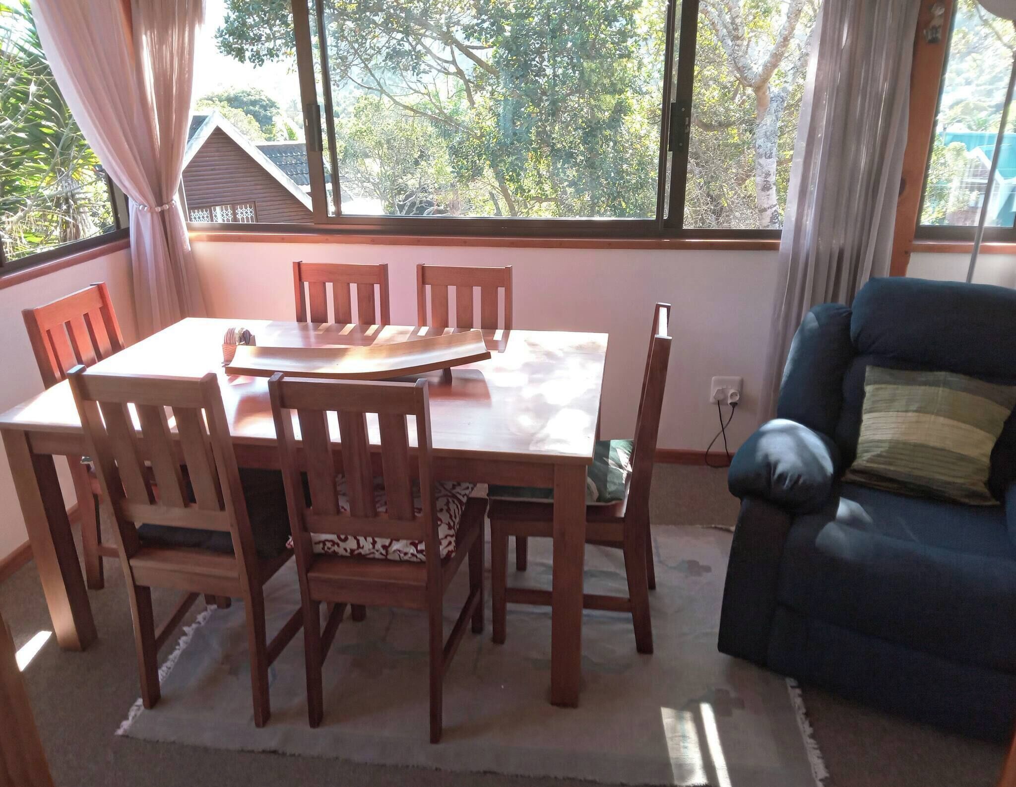 Un comedor con una mesa y sillas, un sofá, y una ventana que ofrece vistas a árboles y un edificio.