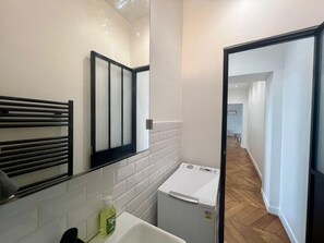 Ein kleines Badezimmer mit Spiegel, Handtuchhalter, Waschmaschine und einer Flasche Handseife.