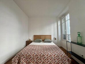 Ein Schlafzimmer mit einem Bett, einem Nachttisch, einem Fenster und einem Regal.