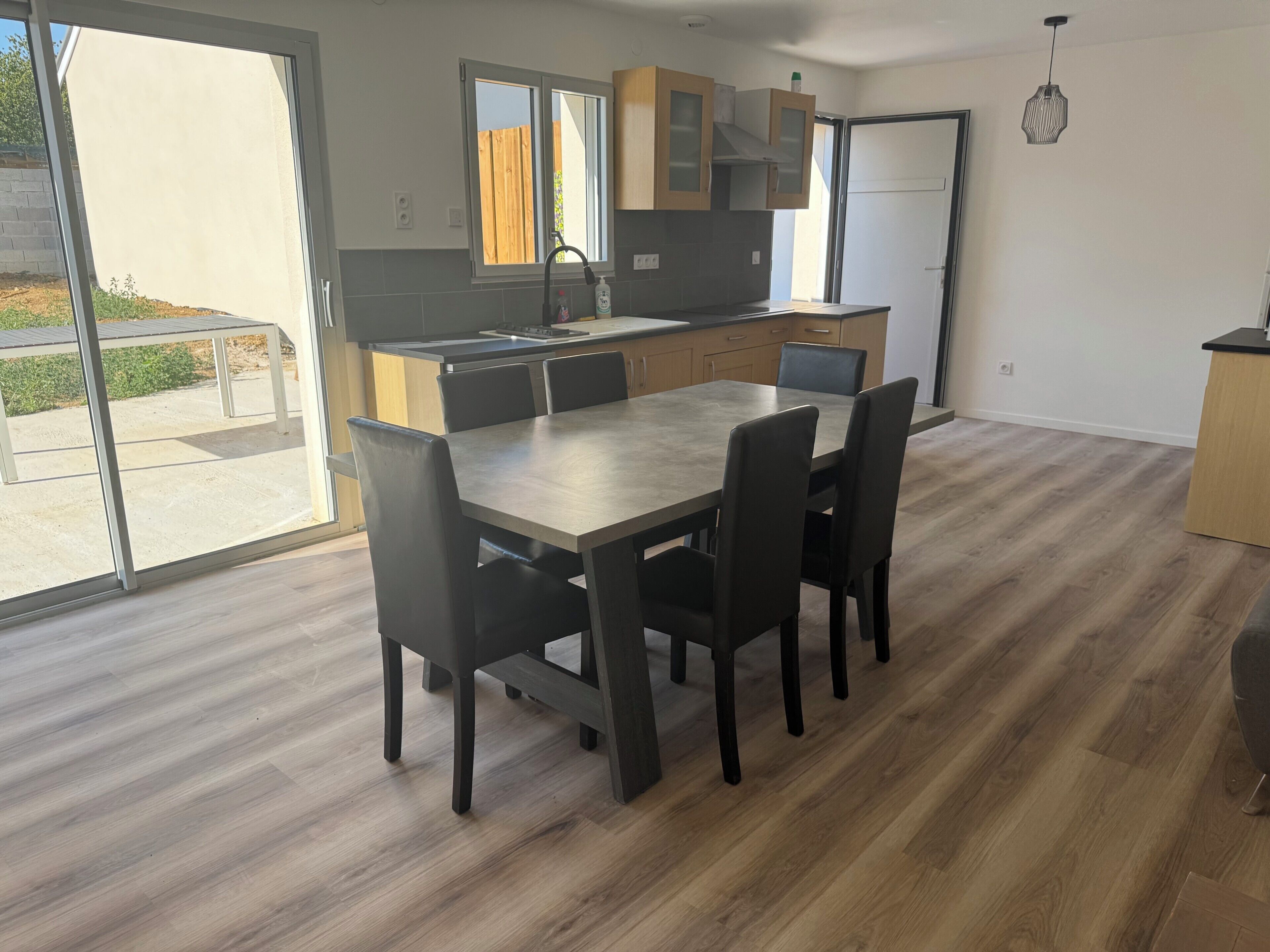 A modern kitchen with a dining area, large windows, and a view of the outdoors.
