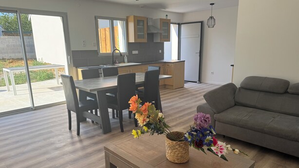 A modern living room with a sofa, dining table, chairs, and a coffee table with flowers. - House with a garden in Saintes (La Clisse)