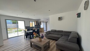 A modern living room with a grey sofa, a wooden coffee table, and a dining area with a table and chairs. - House with a garden in Saintes (La Clisse)