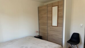 A bedroom with a bed, a black chair, a nightstand, a mirror, and a wardrobe. - House with a garden in Saintes (La Clisse)