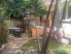 Eine Terrassenanlage mit Whirlpool, Gartenmöbeln und einem kleinen Garten mit Palmen.