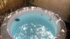 Ett uppblåsbart bubbelbad med blå insida, omgivet av ett bambustaket och en betongmur.