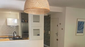 Ett modernt vardagsrum med ett kök, en blå soffa, ett soffbord i glas och en dörr som leder till ett annat rum.