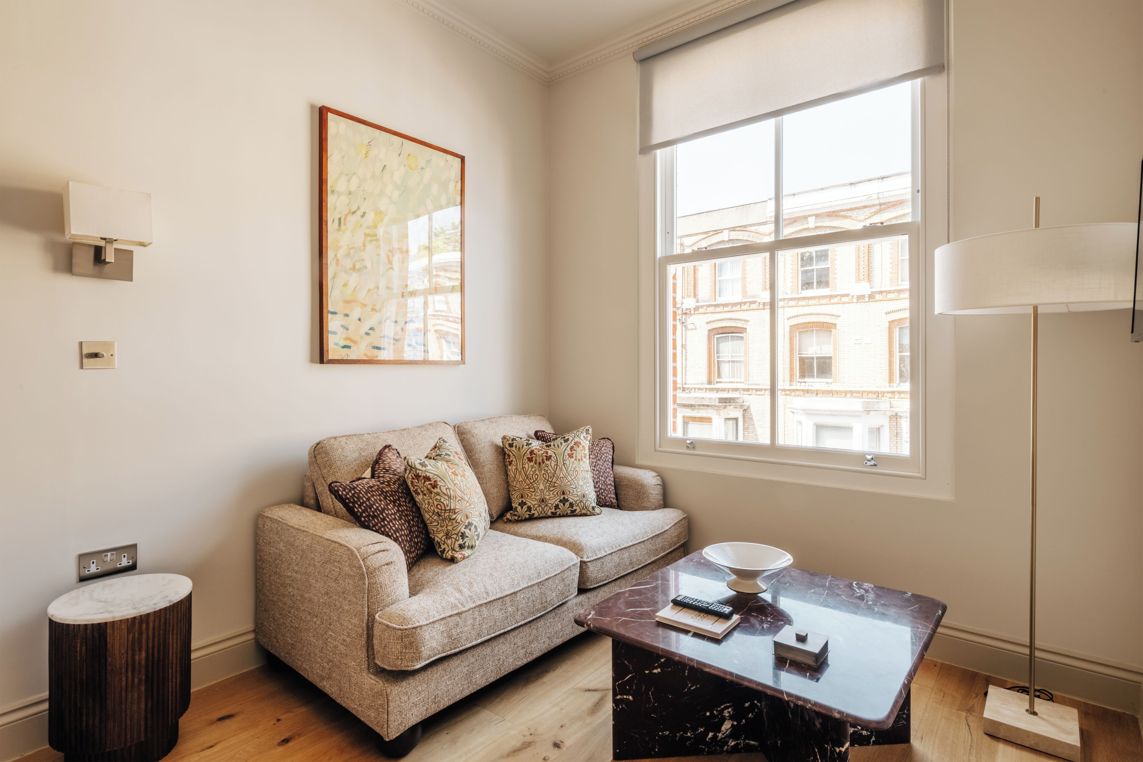 A living room with a sofa, a coffee table, a lamp, and a window with a view of buildings.