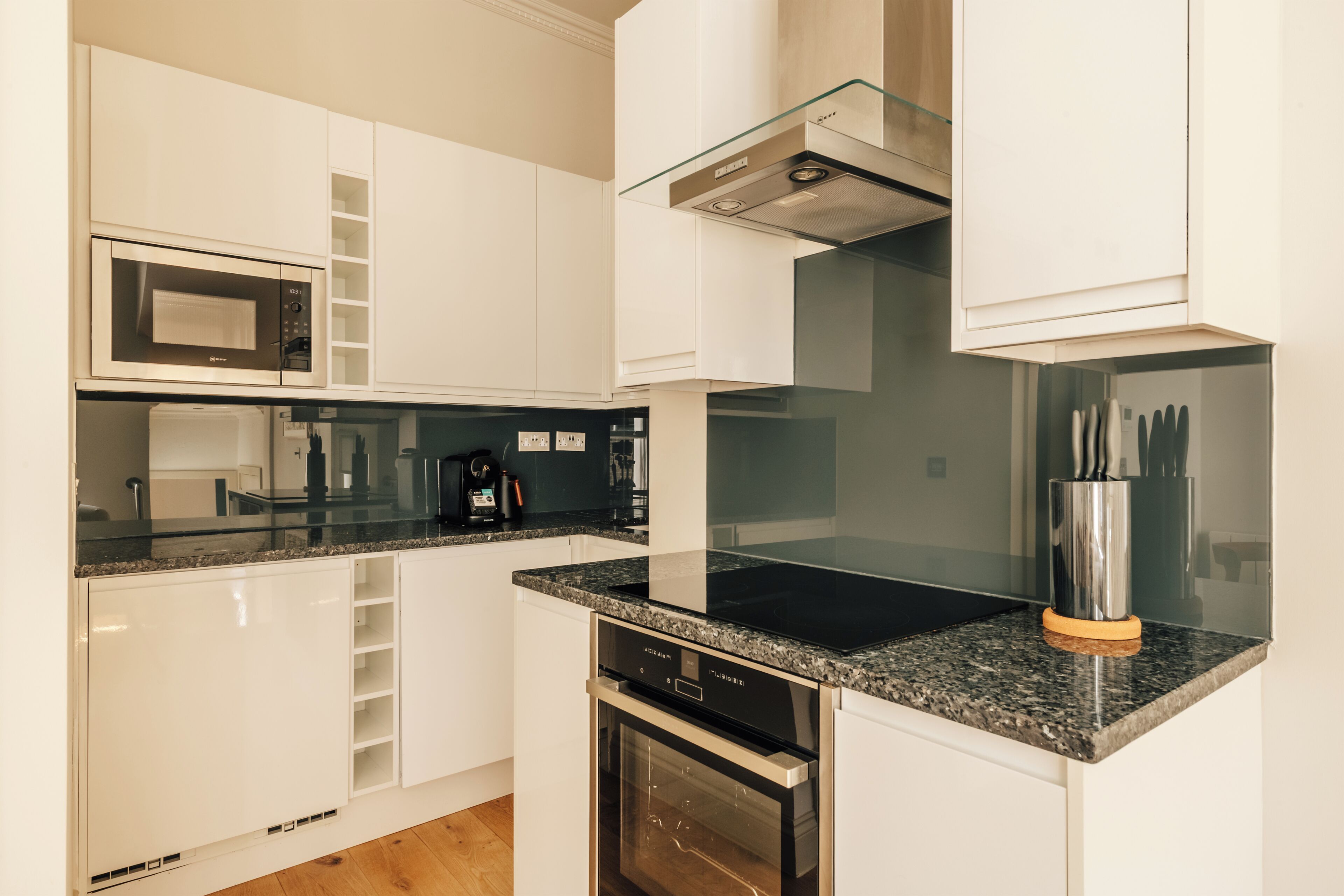 A modern kitchen with white cabinetry, a built-in microwave, a glass stovetop, and a dishwasher.