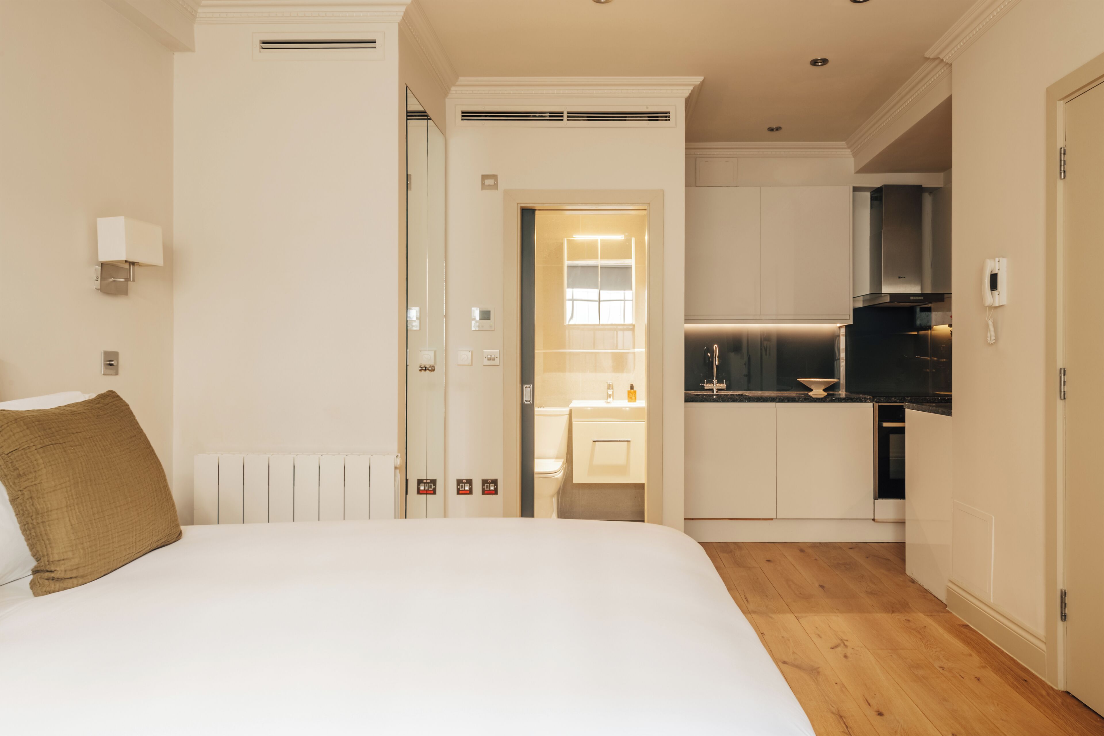 Una habitación de hotel con cama, un pequeño rincón de cocina y un baño visible a través de una puerta abierta.