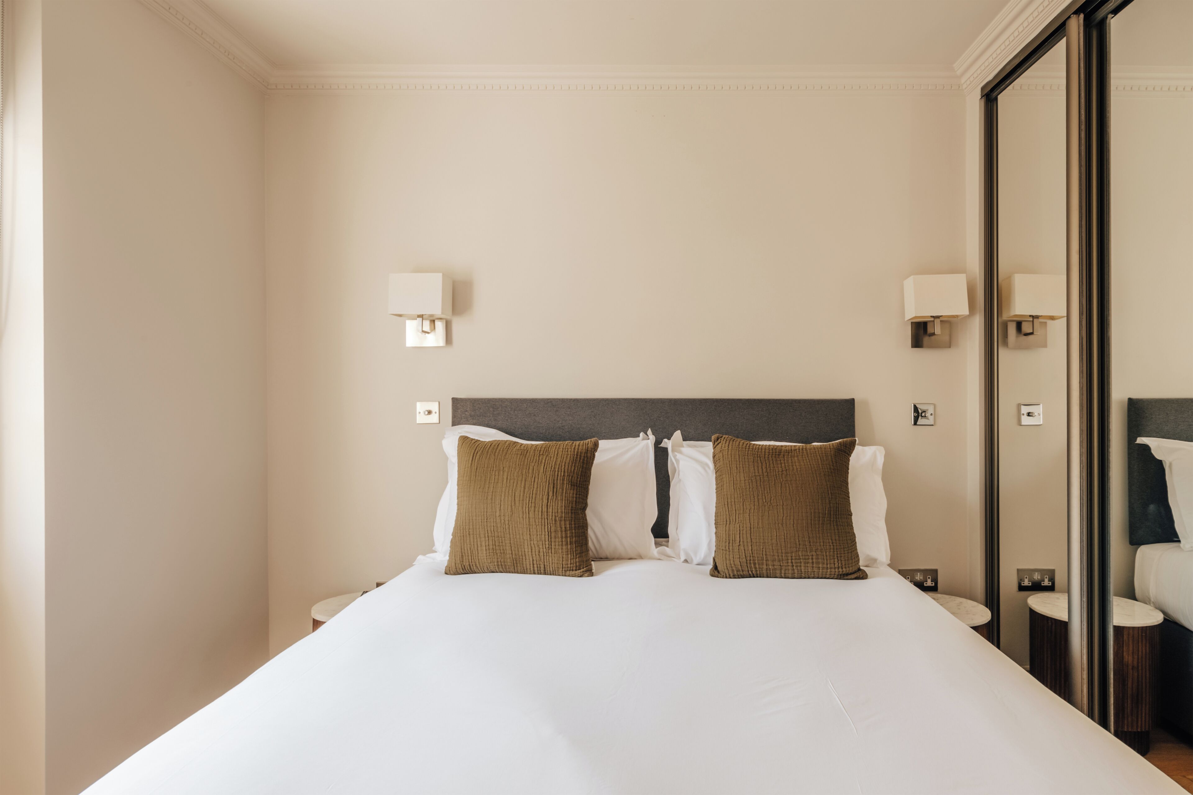 A hotel room with a large bed, two bedside tables, a mirror, and two wall-mounted lamps.