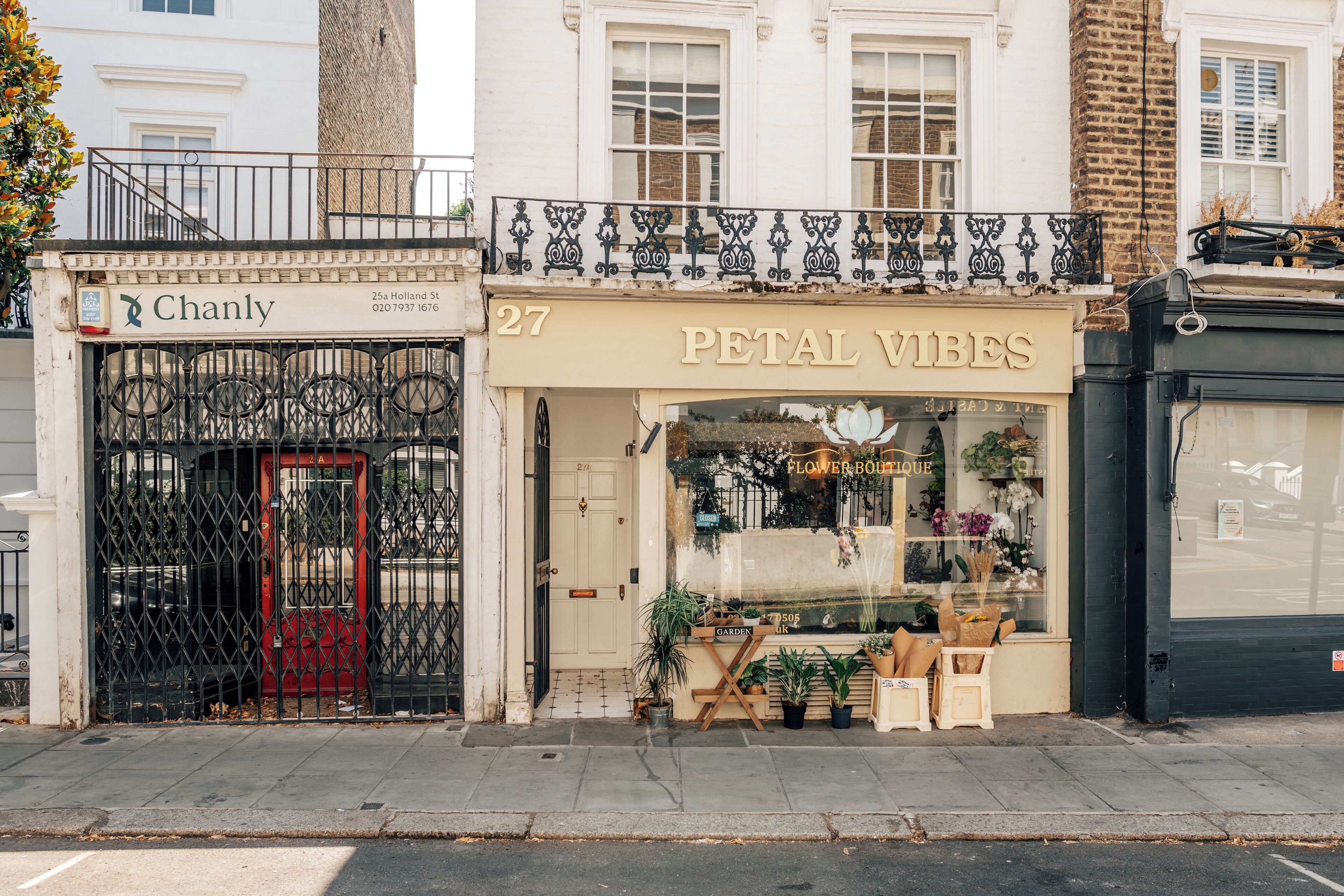 A flower boutique with a closed sign, a red door, and various plants displayed outside.