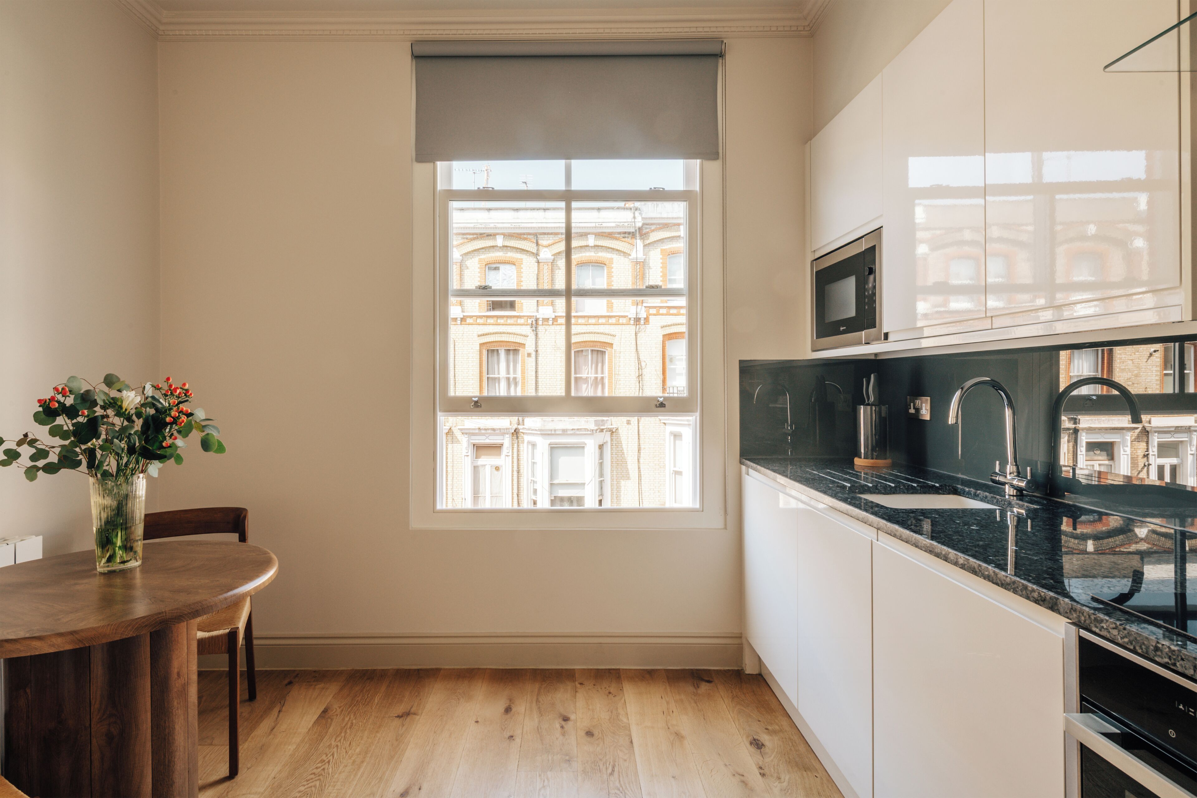 A modern kitchen with a large window, wooden flooring, and a dining area with a table and chairs.