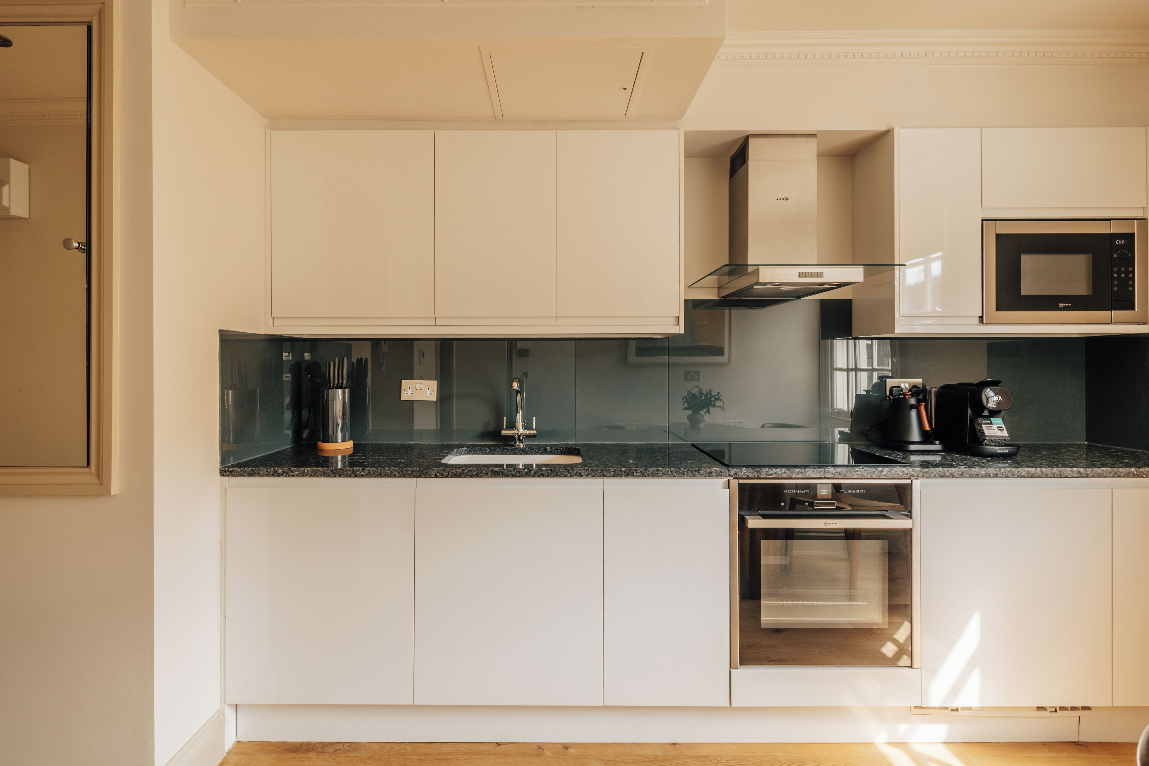 A modern kitchen with white cabinetry, a stainless steel range hood, a built-in microwave, and a dishwasher.