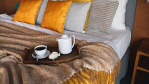 A neatly made bed with a tray of tea and a teapot, accompanied by a fish-shaped salt shaker.