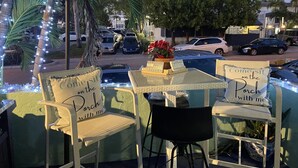 An outdoor seating area with chairs and tables, decorated with lights and a sign that reads "Comesit on the Porch with me."