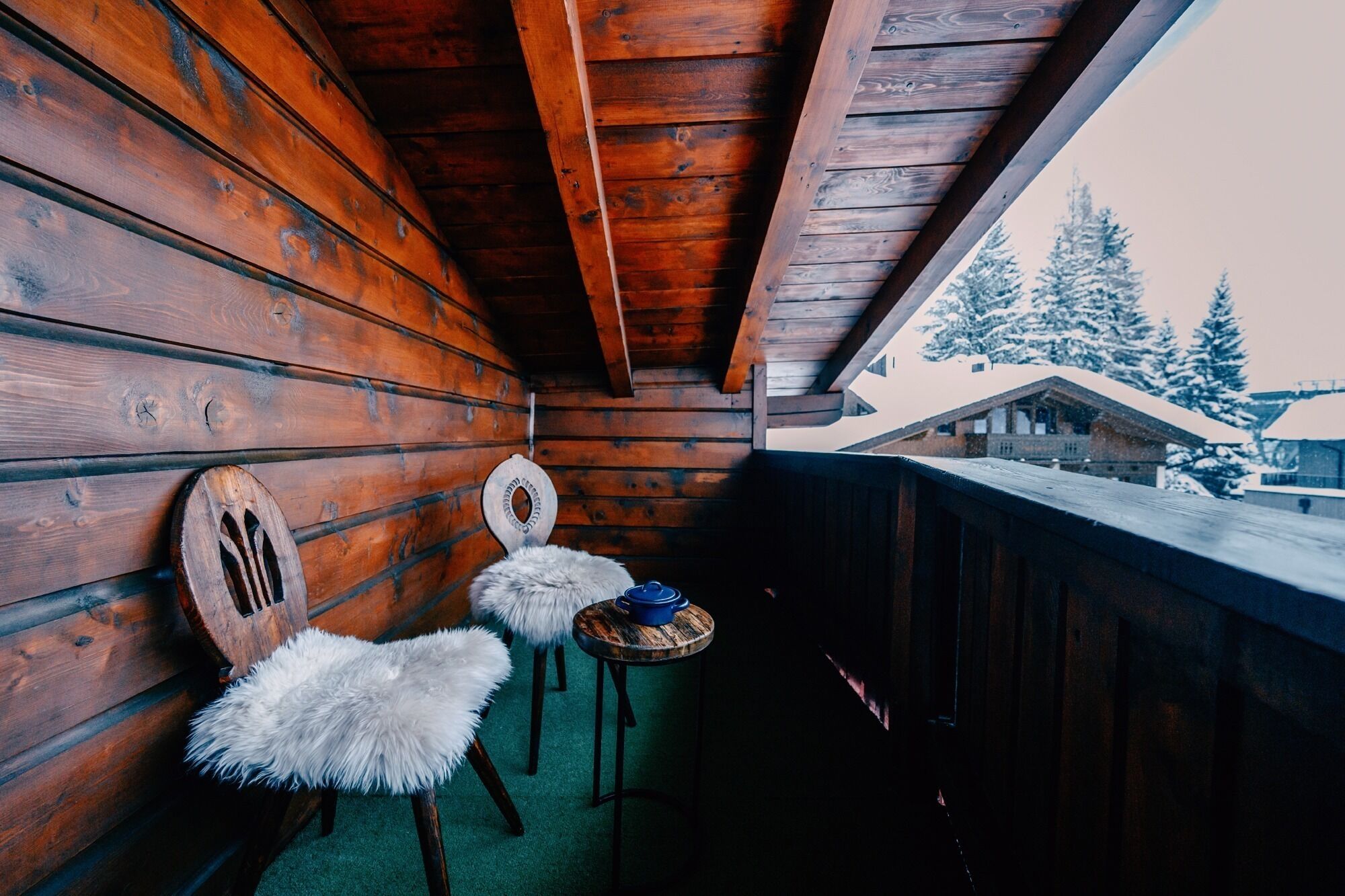 A wooden cabin with a balcony, two chairs, and a table.