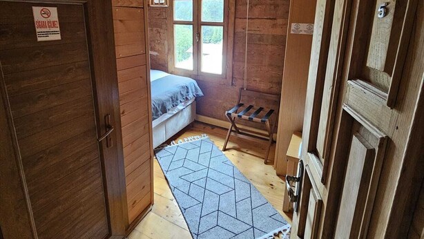 A wooden cabin interior with a bed, a hanging light fixture, a window with a view, and a door with a sign. - hevas suite (çalmlıhemşin)