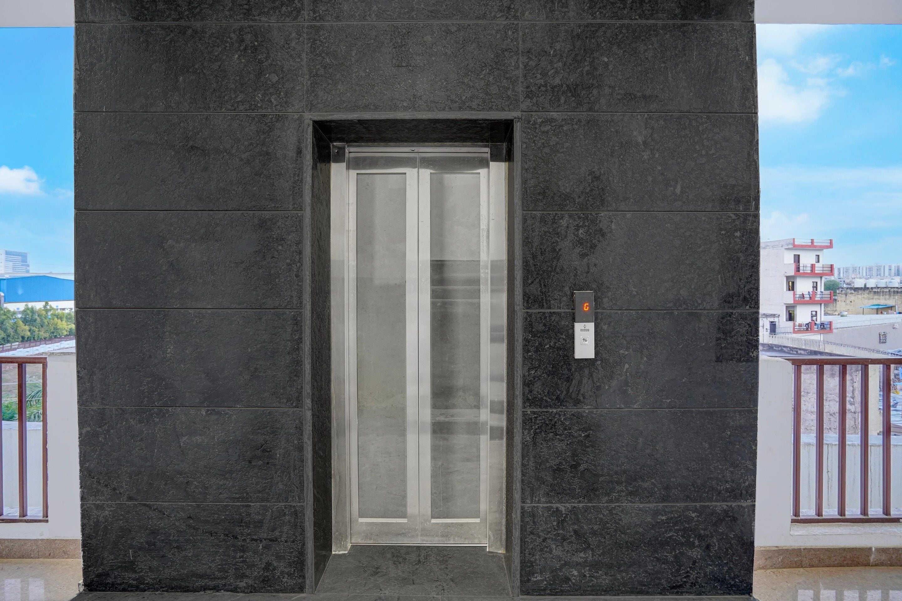 A modern elevator with a glass door, set in a building with dark stone walls.