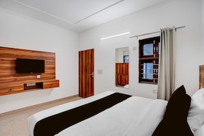 A hotel room with a bed, a flat-screen TV mounted on a wooden panel, a wardrobe, a mirror, and a window with curtains. - Classic With Balcony Hotel Sky (Gurugram)