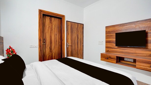 Een hotelkamer met een bed, een televisie bevestigd aan een houten paneel en twee houten deuren.