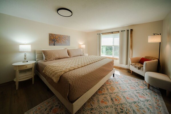 A bedroom with a bed, bedside tables, a chair, a window with curtains, and a painting on the wall.