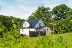 A two-story house with a dark roof, surrounded by lush greenery and trees. - Frog's Landing | Hocking Hills, Hot Tub, Firepit (McArthur)