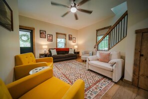 A living room with a sofa, armchairs, a coffee table, a patterned rug, a ceiling fan, and a staircase. - Frog's Landing | Hocking Hills, Hot Tub, Firepit (McArthur)