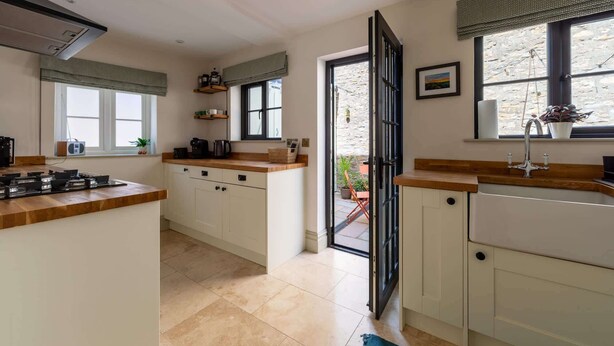 A kitchen with white cabinets, a wooden countertop, a gas stove, and a view of the outside. - Gorgeous Georgian Townhouse in Central Frome (Somerset)
