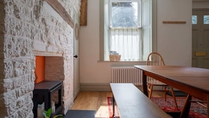 A room with a stone wall, a fireplace, a dining table, and a window with curtains. - Gorgeous Georgian Townhouse in Central Frome (Somerset)